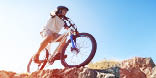 Mountain biker in action across rocks against blue sky concept for healthy lifestyle, excercise and extreme sports